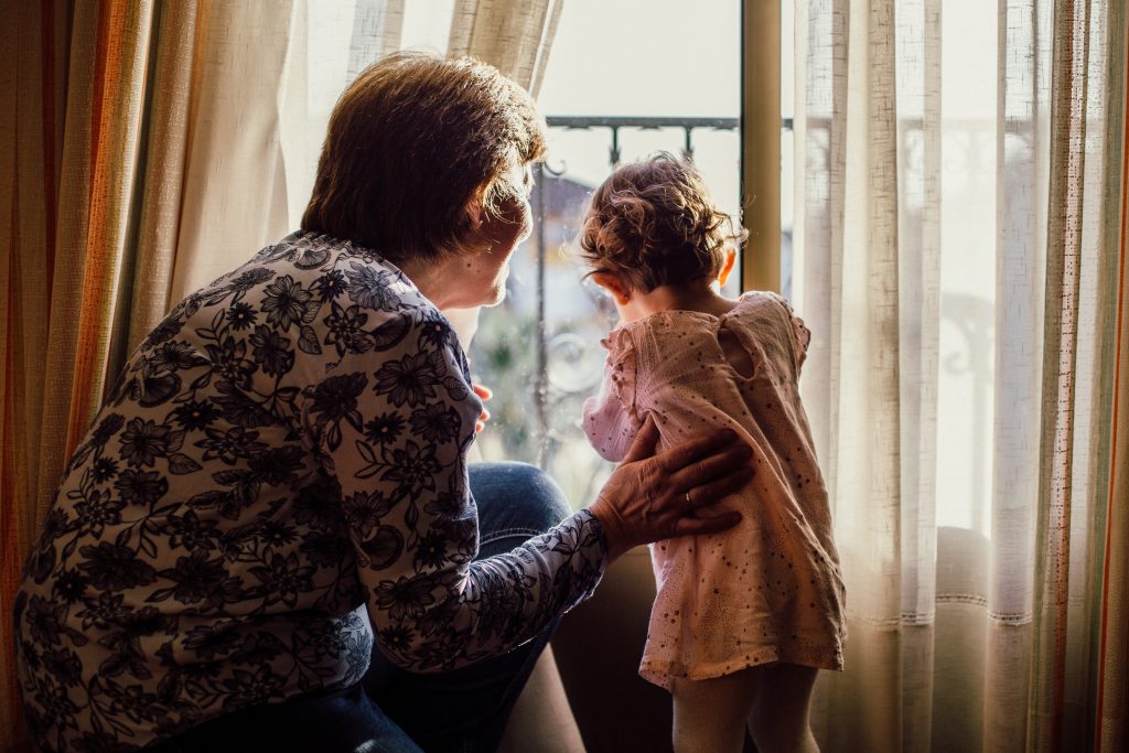 A grandmother with her grandson are standing on the windowsill looking at the street